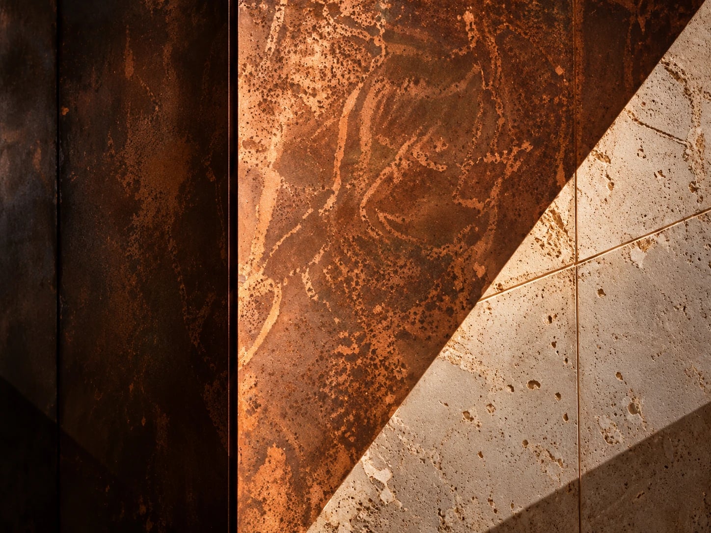 A weathered copper-toned steel panel meeting pale natural stone along a sharp diagonal